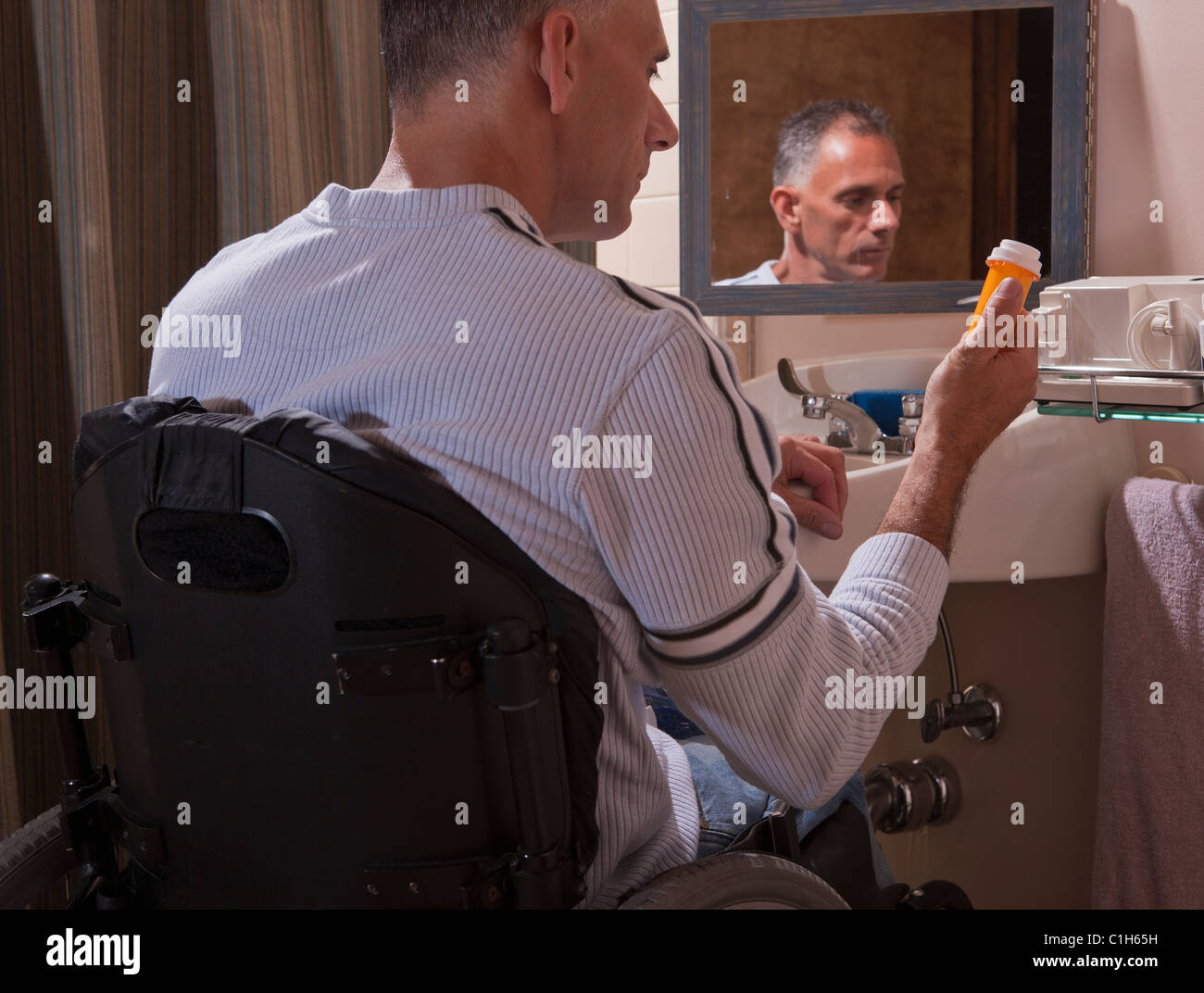 Man with spinal cord injury in a wheelchair looking at a pill bottle