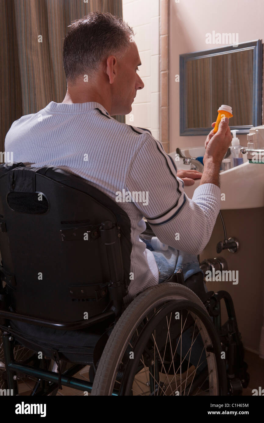 Man with spinal cord injury in a wheelchair looking at a pill bottle