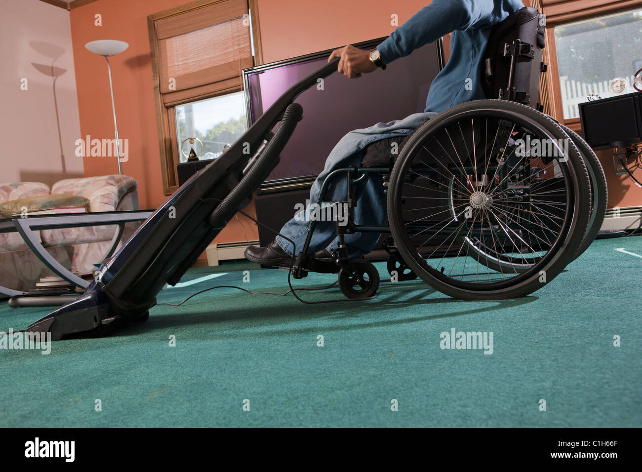 Man with spinal cord injury in a wheelchair using a vacuum cleaner at