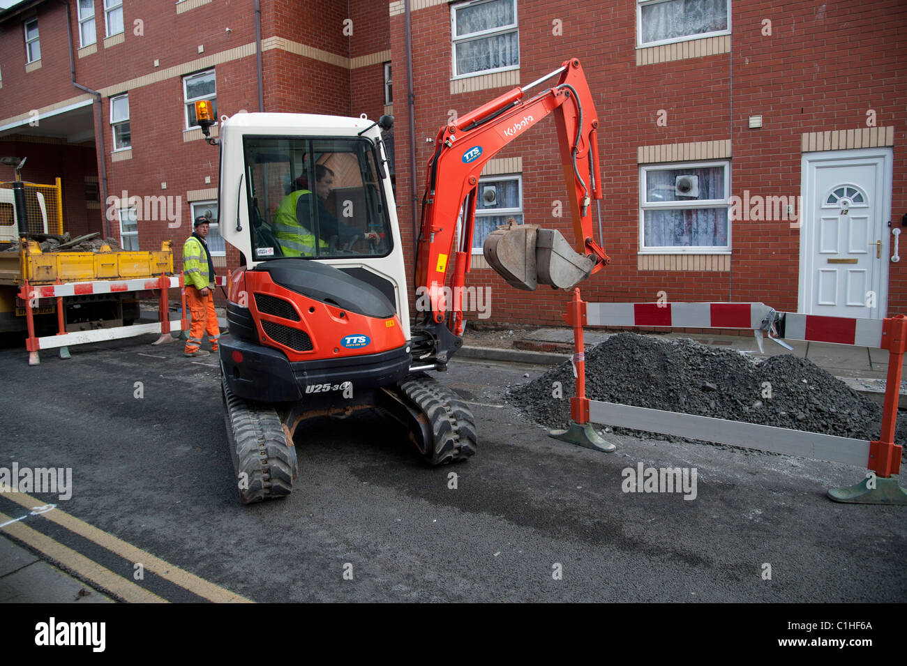 A mini digger excavating on a street, replacing old pavement, UK Stock Photo