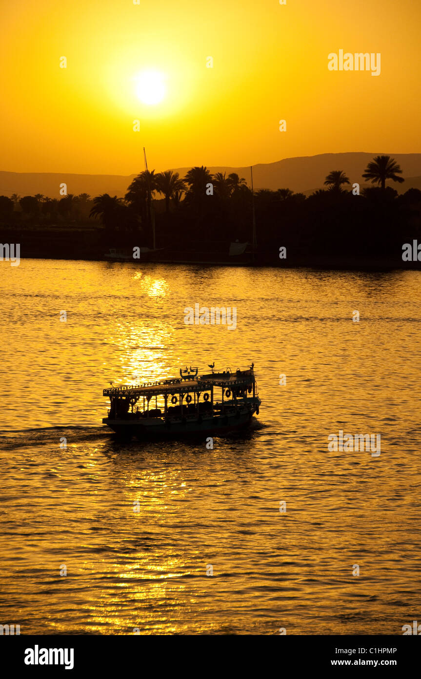 A traditional Egyptian Felucca Boat sails on the Nile in Luxor, Egypt with a passenger ferry passing. Stock Photo