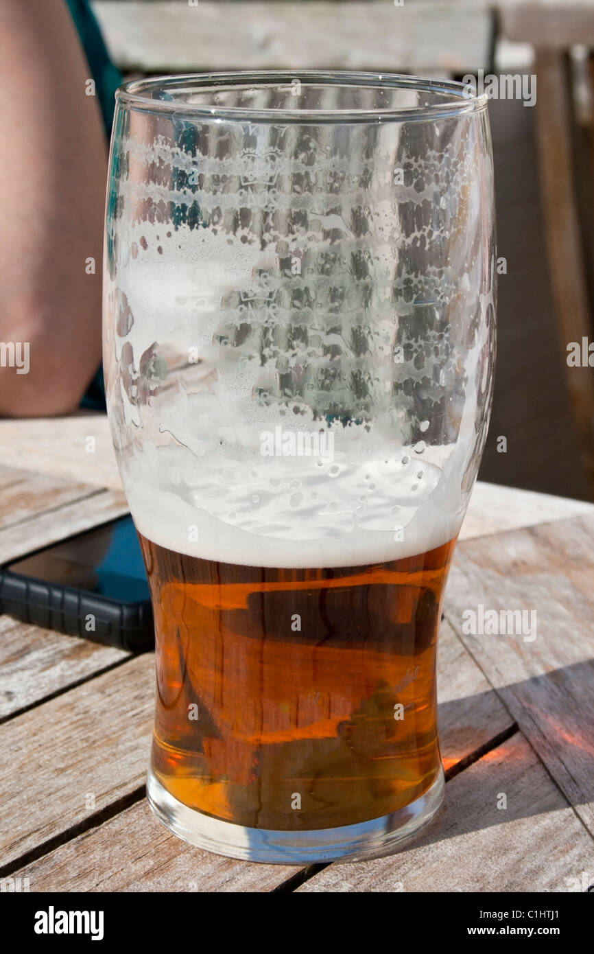 english bitter ale with head, beer garden table, next to mobile phone Stock Photo