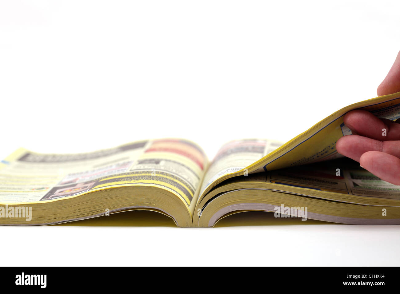 Hand turning over a page of the yellow pages, white background - shallow depth of field. Stock Photo