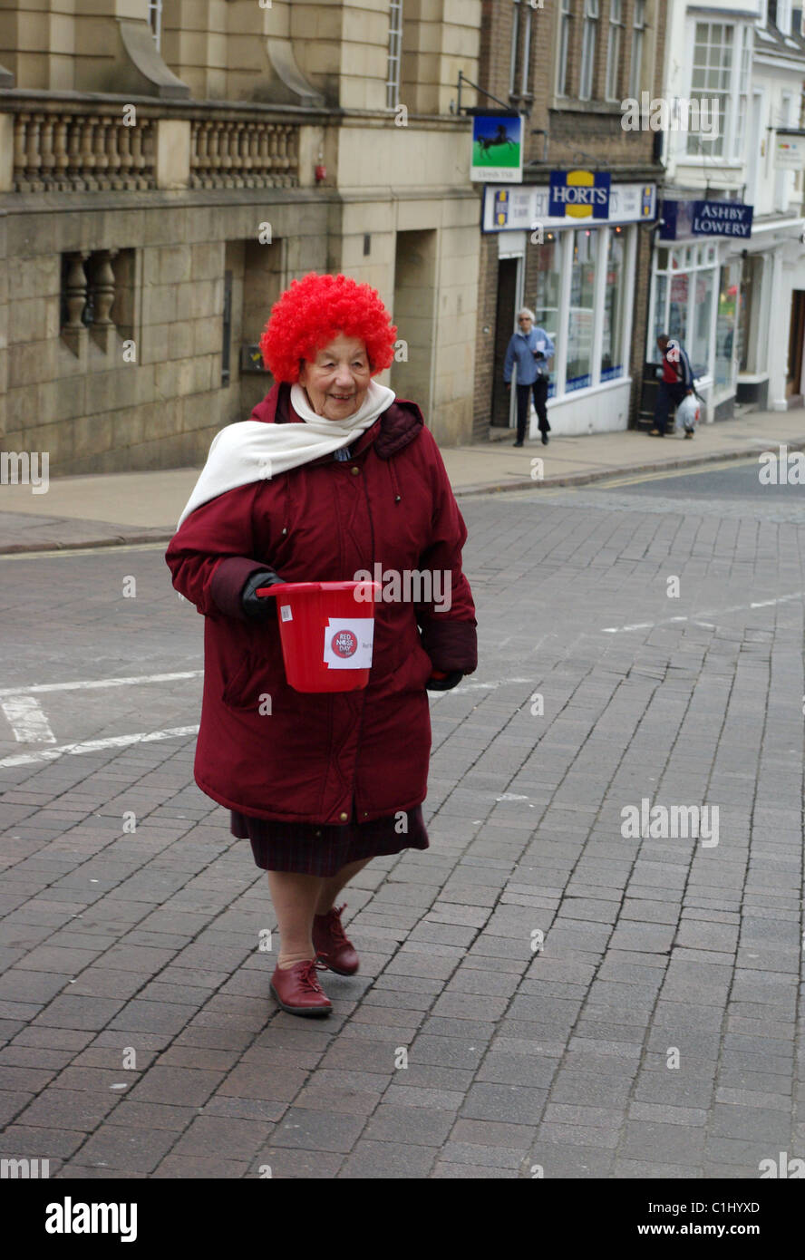 Older woman in red coat and red wig collecting money for Comic Relief Stock Photo