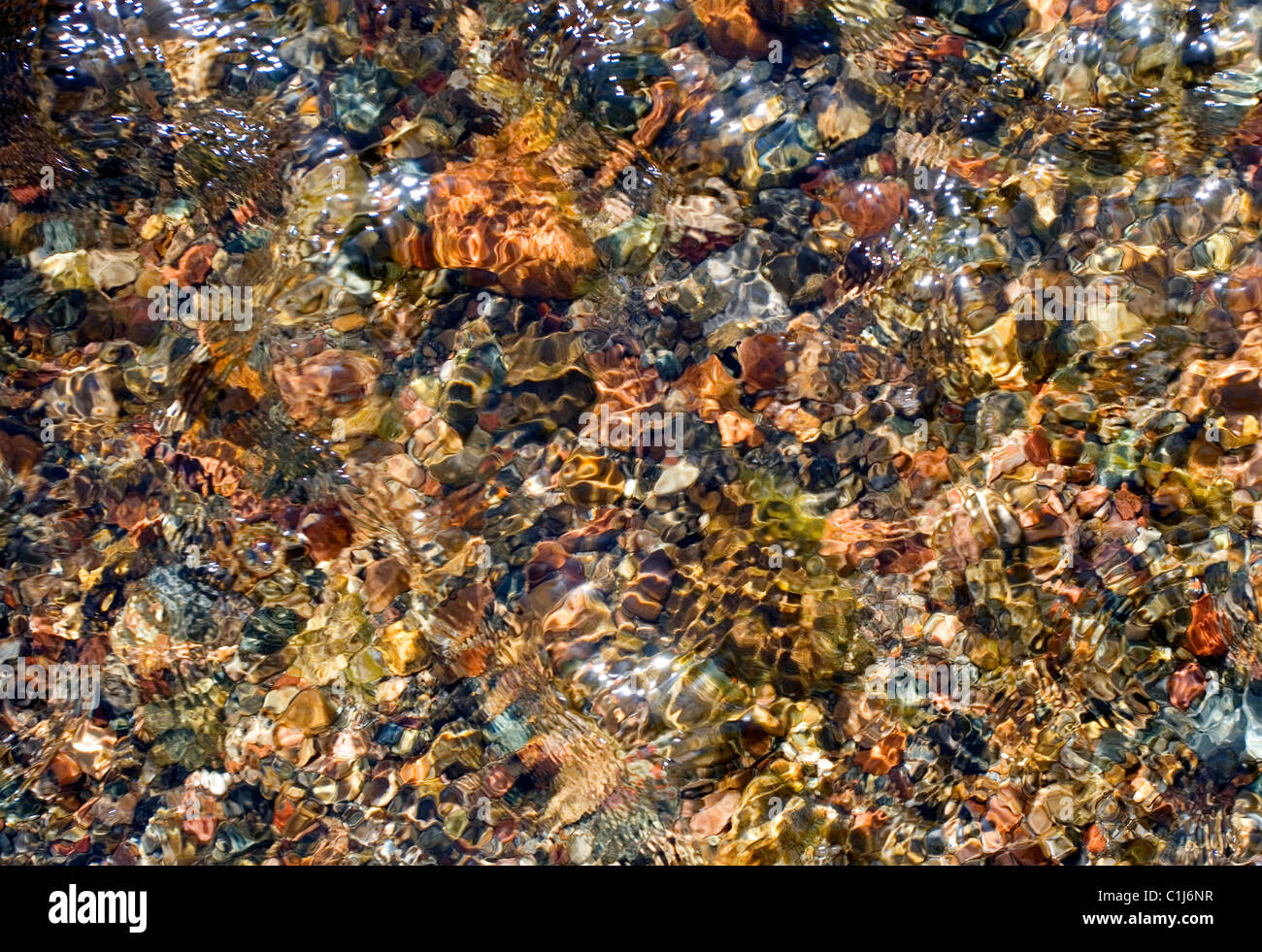Looking straight down into a shallow stream of fresh cool water and colorful stones and pebbles. This stream is small tributary Stock Photo