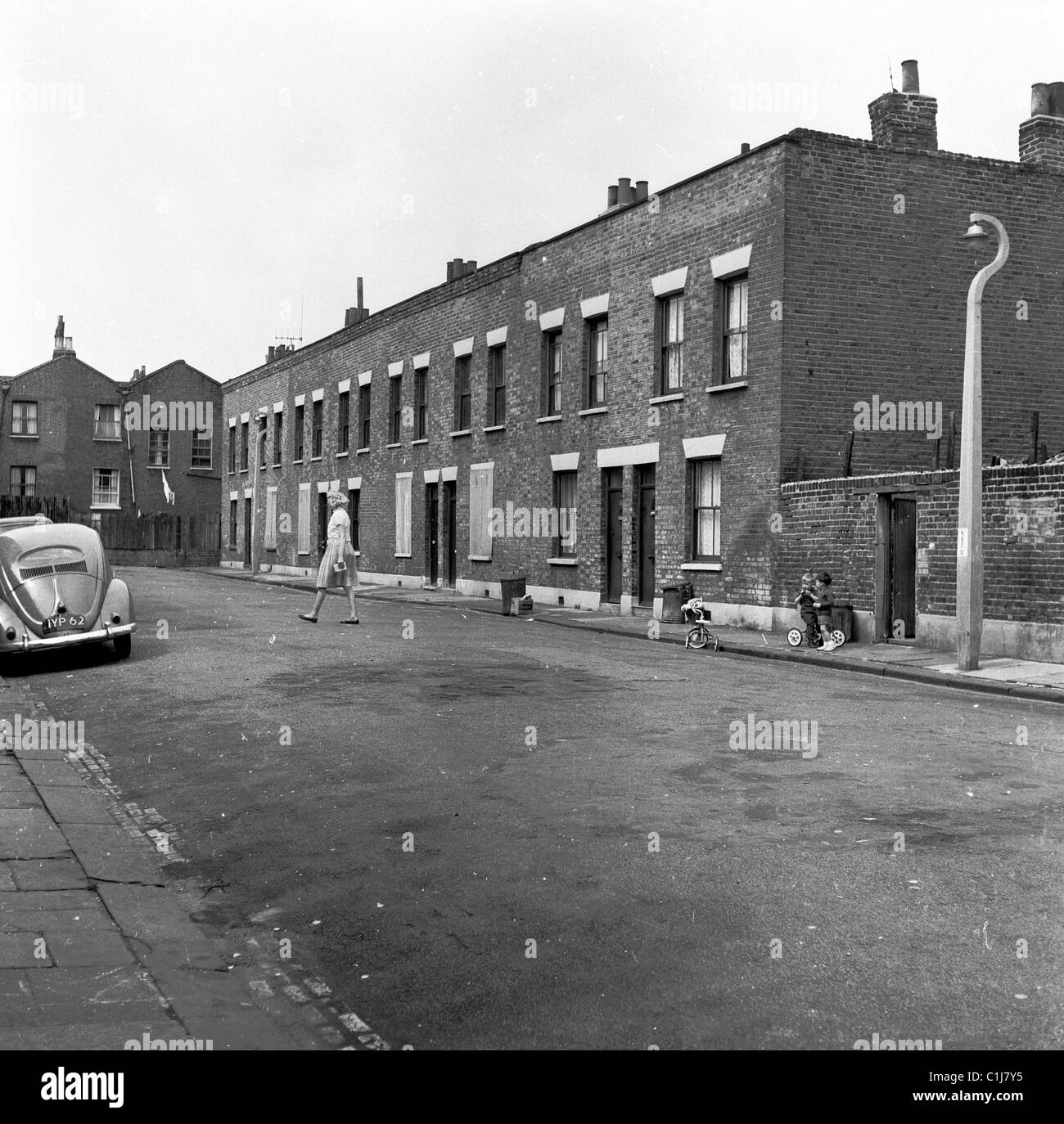 1950s. Historical. Small children play in an empty inner-city London street outside a row of small old victorian terraced houses. Stock Photo