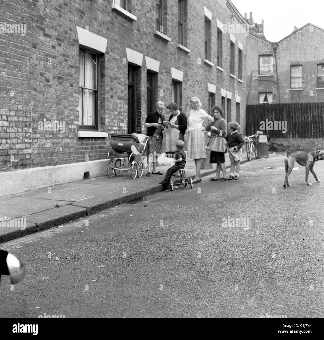 1950s, London, England, historical, victorian terraced houses, small group of mothers outside in the street with their children, pram, and tricycle. Stock Photo