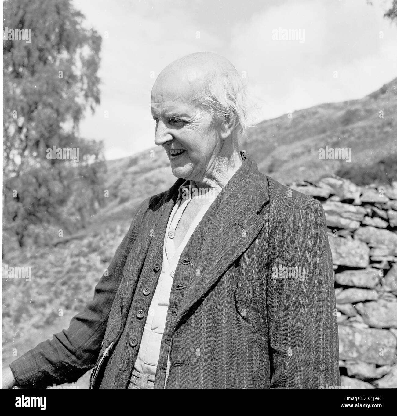 1950s, historical, an elderly man in old, ragged waistcoat and suit jacket standing by a stone wall, a traditional country traveller, England, UK. Stock Photo