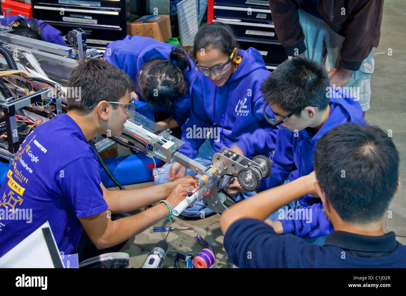 This image shows multi ethnic teen girls and guys working as a team on a robot, wearing safety glasses. Robotic competition. Stock Photo