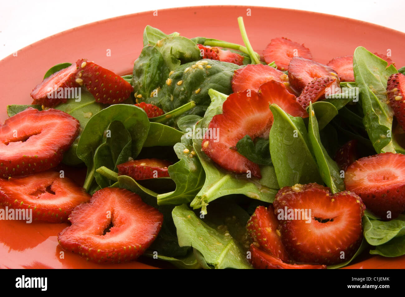 This closeup is of a fresh spinach and strawberry salad on a red plate. Also has sesame seeds and garlic for a delicious side. Stock Photo