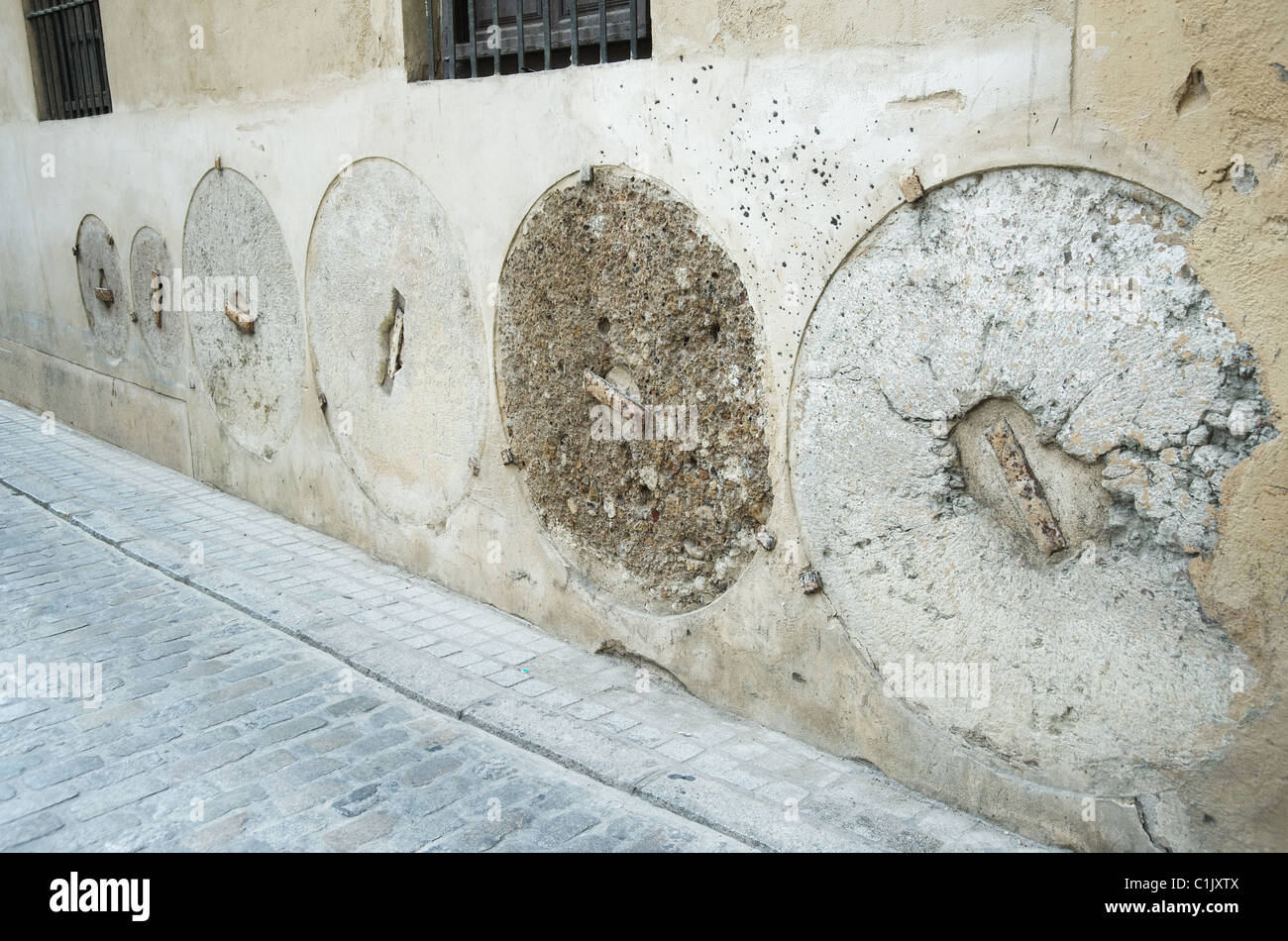 Mill stones embedded in building wall on narrow lane in city center. Seville, Andalusia, Spain. October 2010. Stock Photo