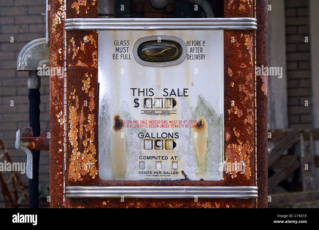 Old, rusty, vintage American gas pump in front of a brick wall with fence. Stock Photo