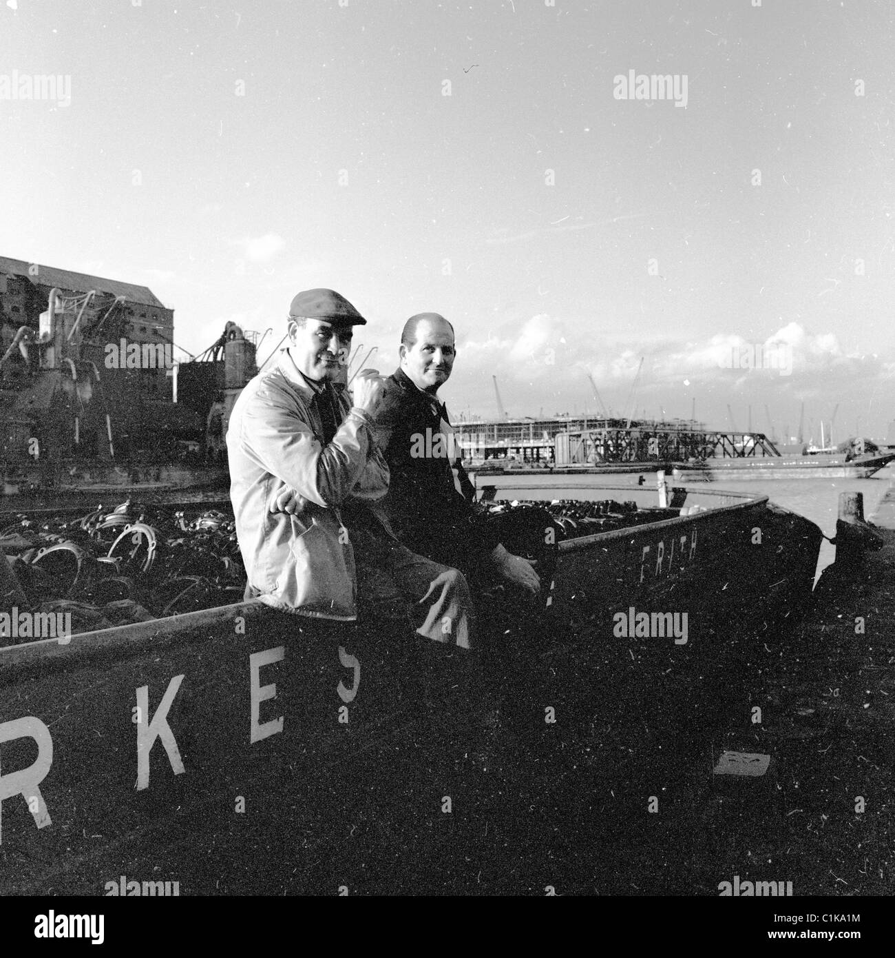 Two dockers take a break sitting on a tug boat at Millwall Dock, East End of London, in this picture taken in the 1950s. Stock Photo