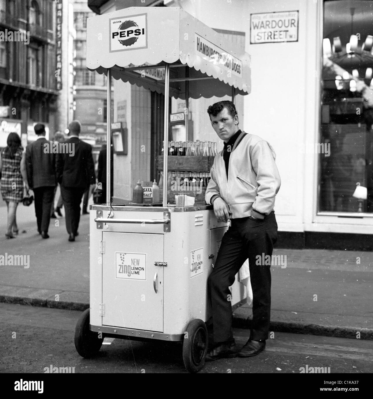 196s, London. Portable hot dog stand ans seller on the corner of