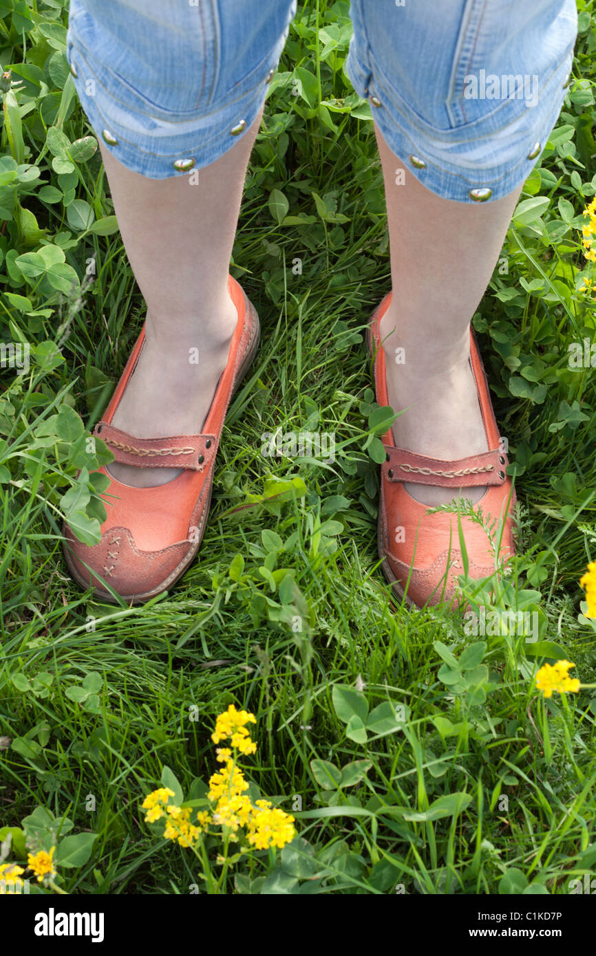 Feminine legs in orange loafer on green herb Stock Photo