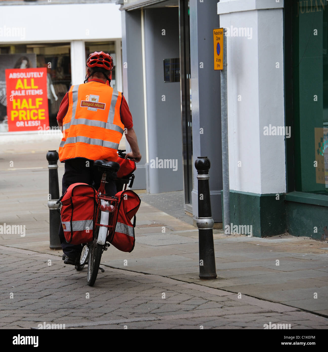 Postman riding a bicycle with pannier bags on his town centre round in Evesham England UK Stock Photo