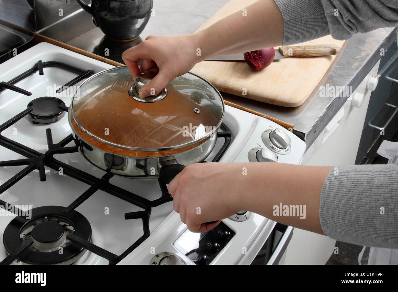 Putting a lid on a saucepan of simmering chicken rogan josh Stock Photo