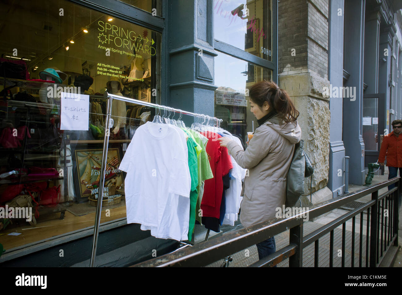 A young woman browses a rack of sale tee shirts outside of a thrift store in Soho in New York Stock Photo