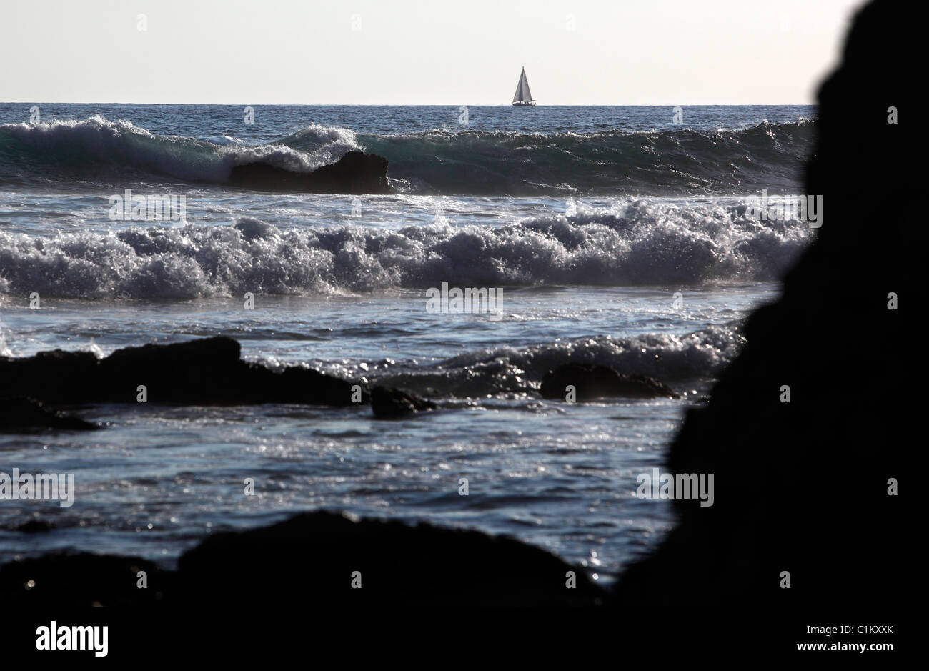 Waves break on a rocky coast with a sailboat on the horizon, Samara, Nicoya Peninsula, Costa Rica Stock Photo