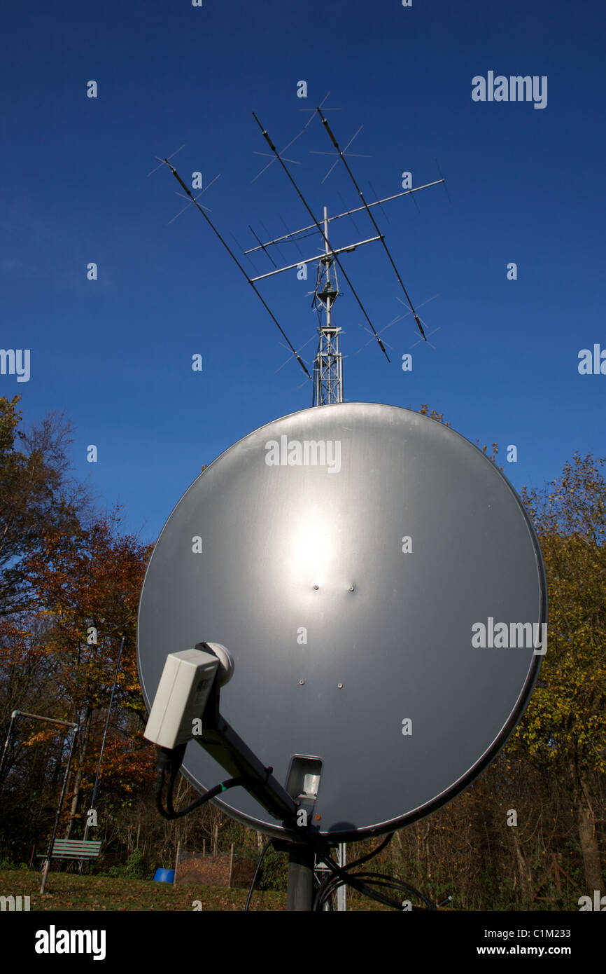 Satellite Dish and Yagi Amateur Radio Antenna Display set against a blue cloudless sky and trees in portrait format Stock Photo