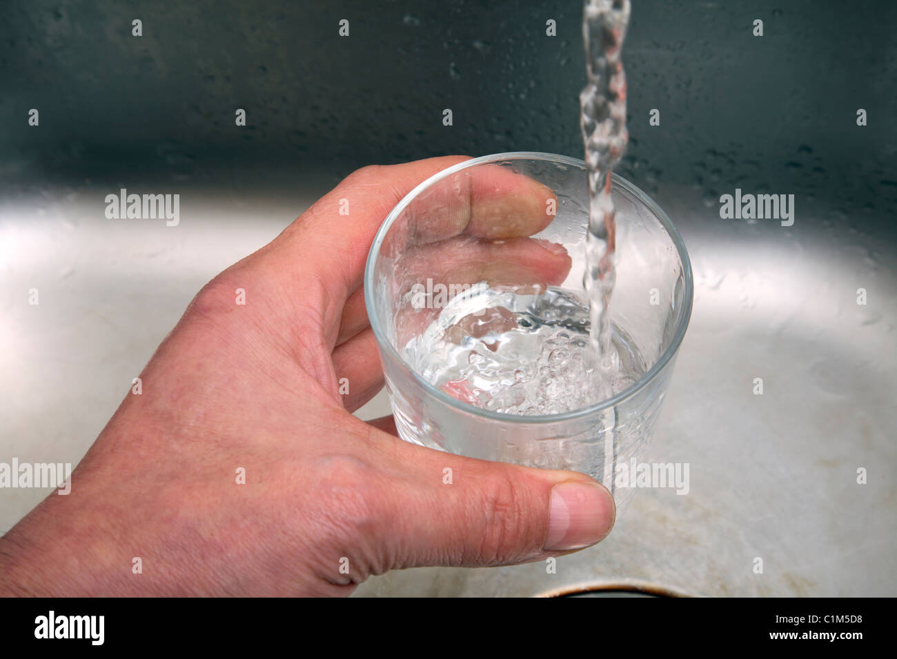 Man filling a glass with water from a kitchen tap. Stock Photo