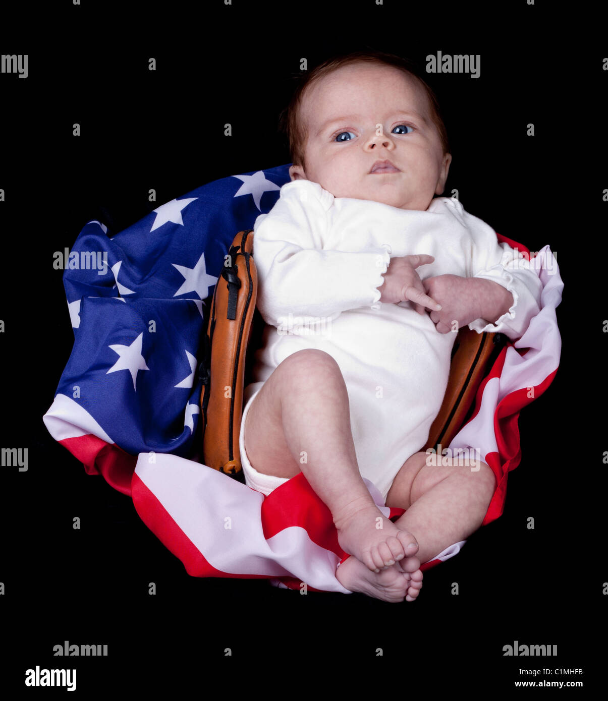 An adorable baby in a baseball glove on a flag. There is a black