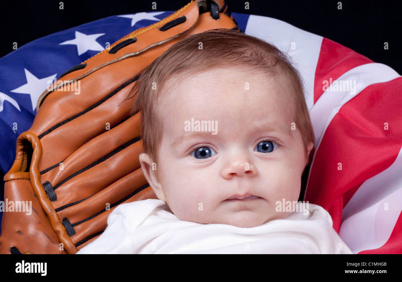 A baby leaning against an American Flag and a baseball glove. Stock Photo