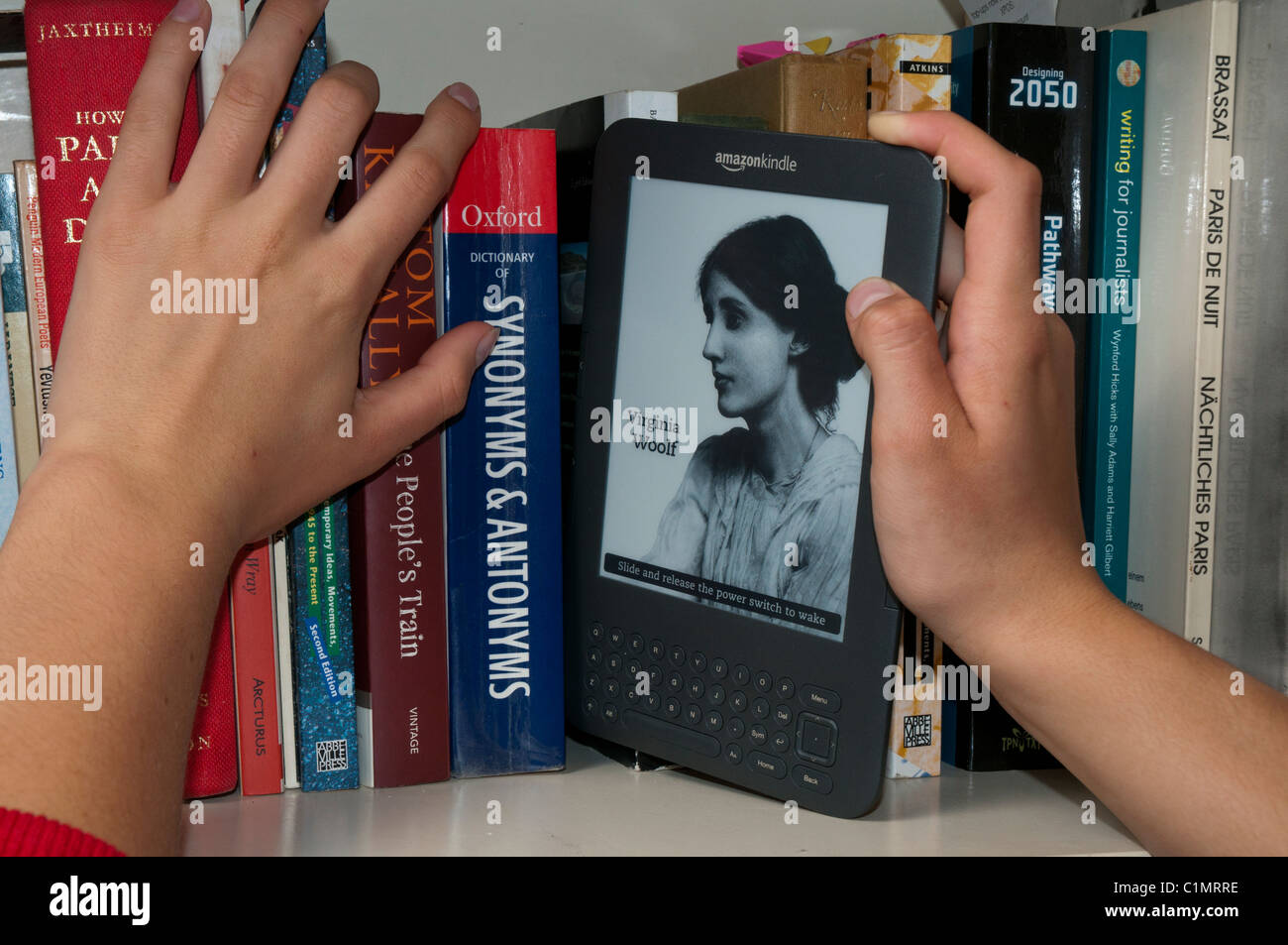 A Kindle model 3 ebook reader being inserted iamongst traditional print books on a bookshelf Stock Photo