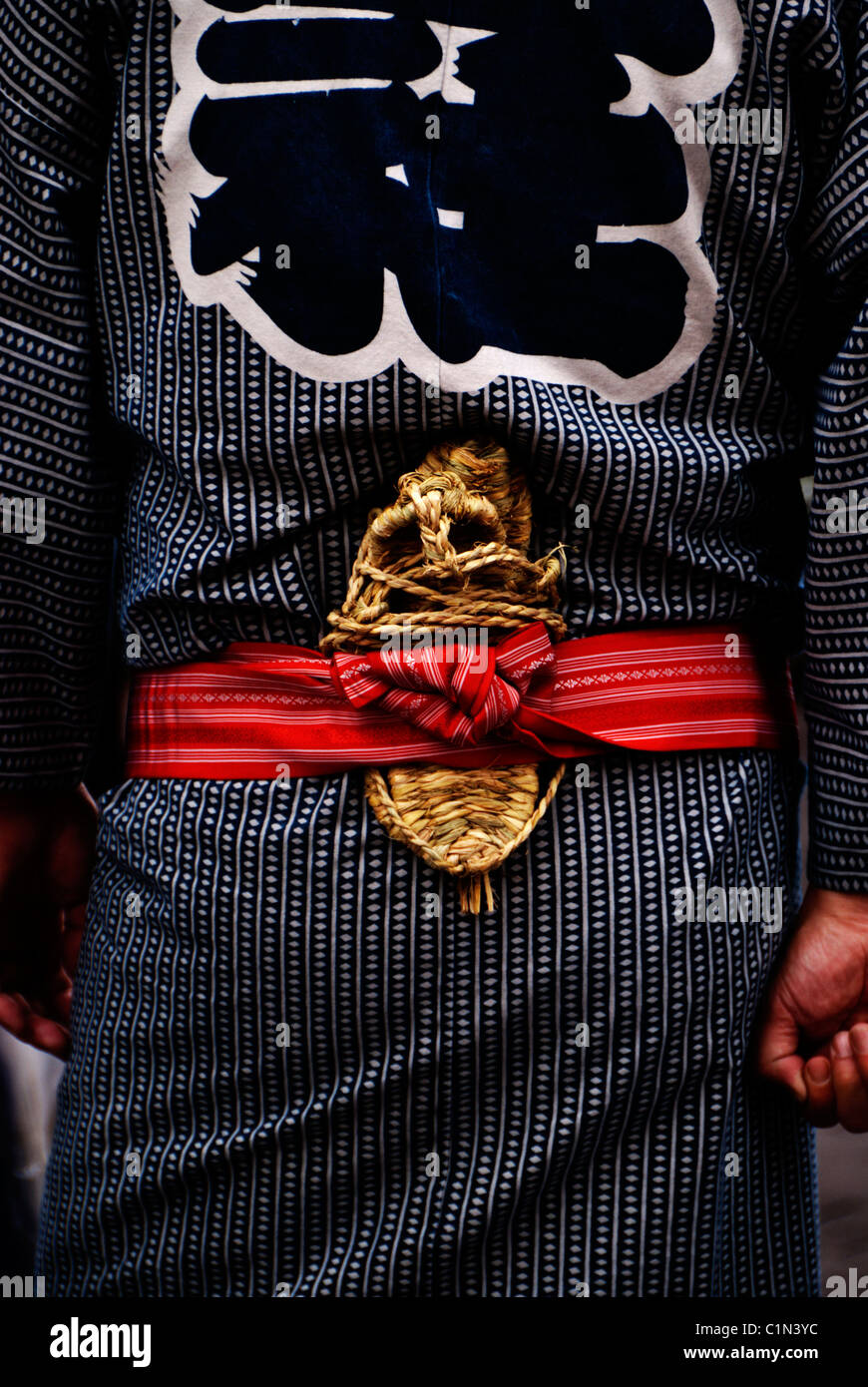 A Japanese man wears a traditional blue yukata kimono with a red obi and has straw sandals (zori) tucked into his belt. Stock Photo