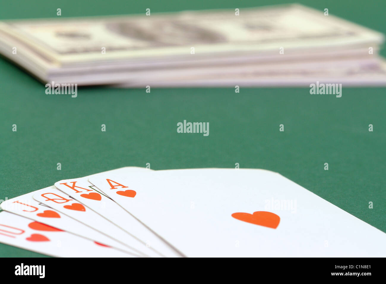 Royal flush cards put on green table cloth with pile of dollars in the background Stock Photo