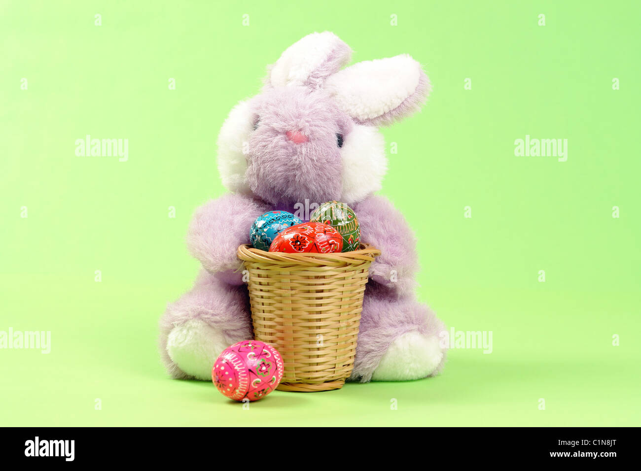 Easter bunny sitting with wooden basket full of easter eggs over light ...
