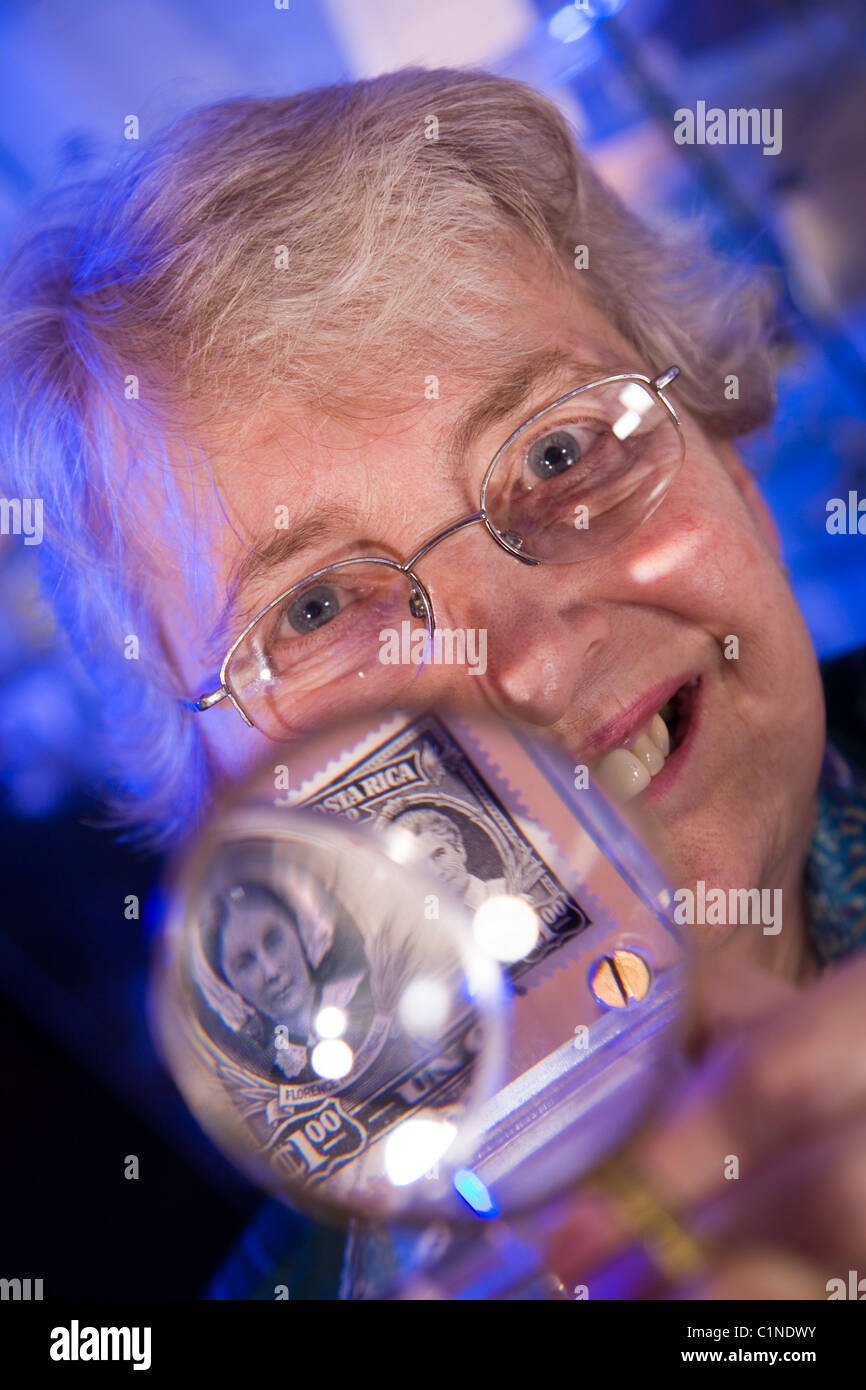 A mature woman / retired female / senior / stamp collector / philatelist with some magnified old / collectable postage stamps. Stock Photo