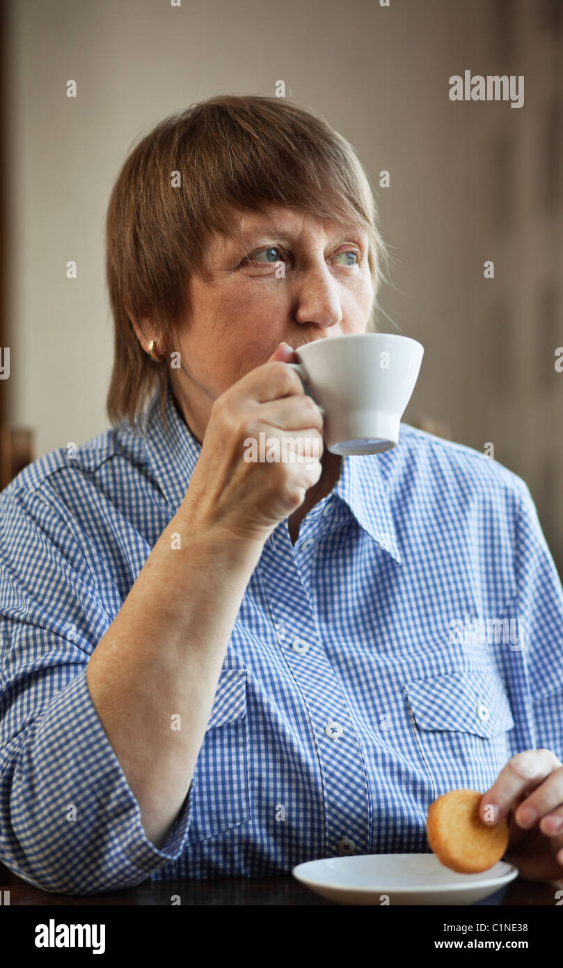 Elderly woman enjoying a cup of coffee and cookie at home Stock Photo