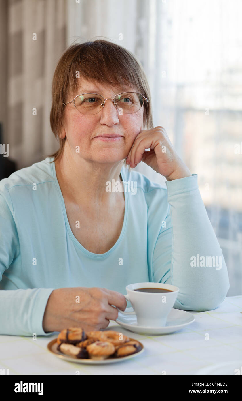 Elderly woman enjoying a cup of coffee with cookies at home Stock Photo