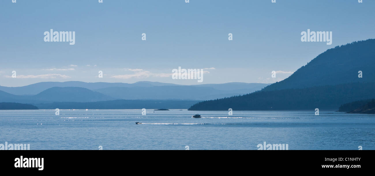 Gulf Islands silhouetted against strong light with small boats, British Columbia, Canada Stock Photo