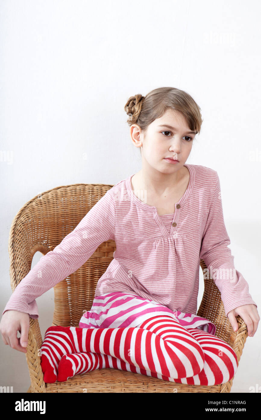 Calm little girl sitting on chair and looking ahead Stock Photo - Alamy