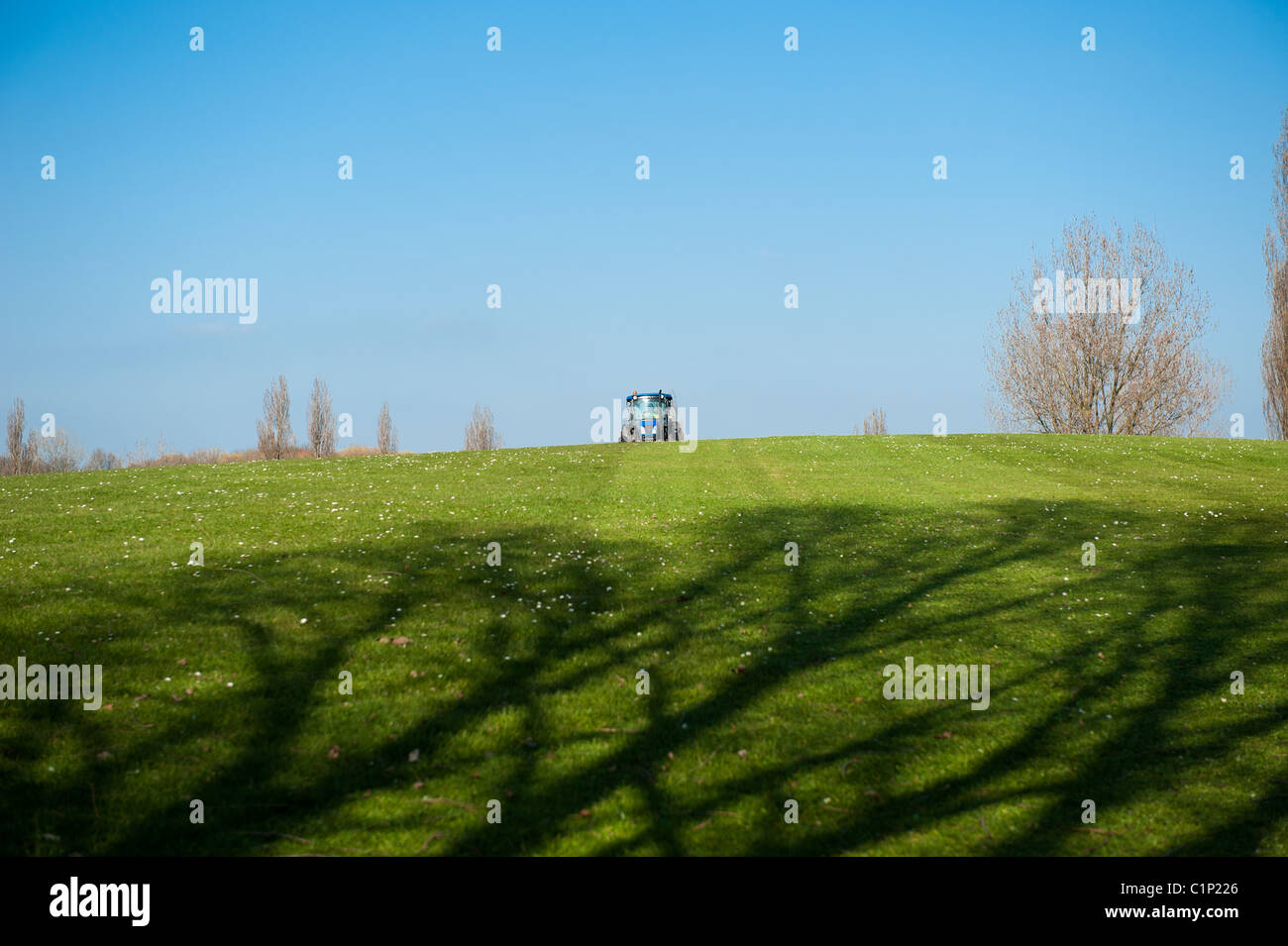 A council tractor approaches as it cuts the grass in a council run park in Basildon, Essex. UK. Stock Photo