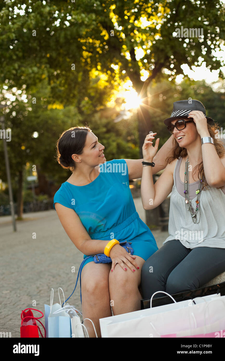 Two women sitting on bench with shopping bags, smiling Stock Photo