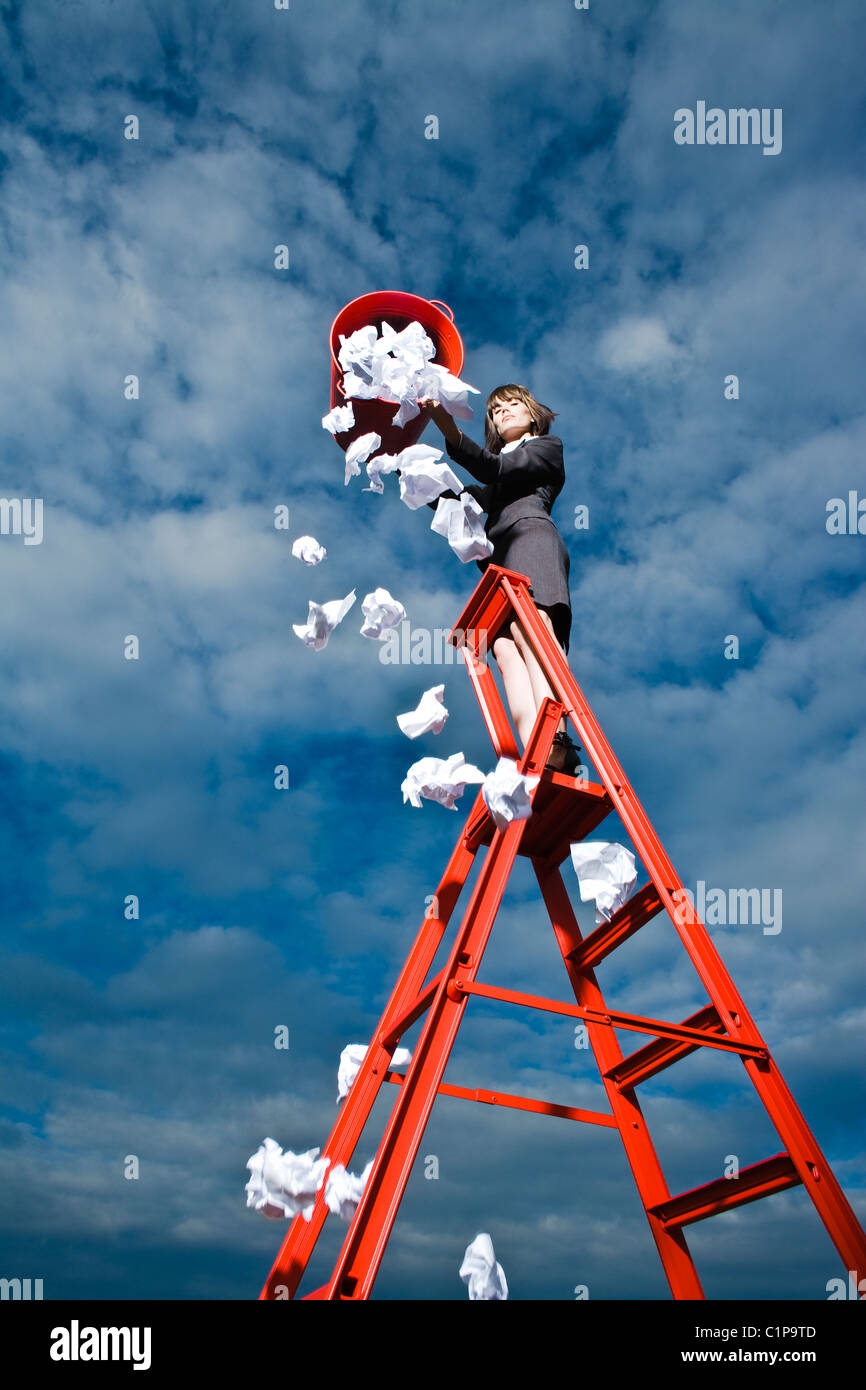 Woman throwing out rubbish from red bin standing on ladder Stock Photo