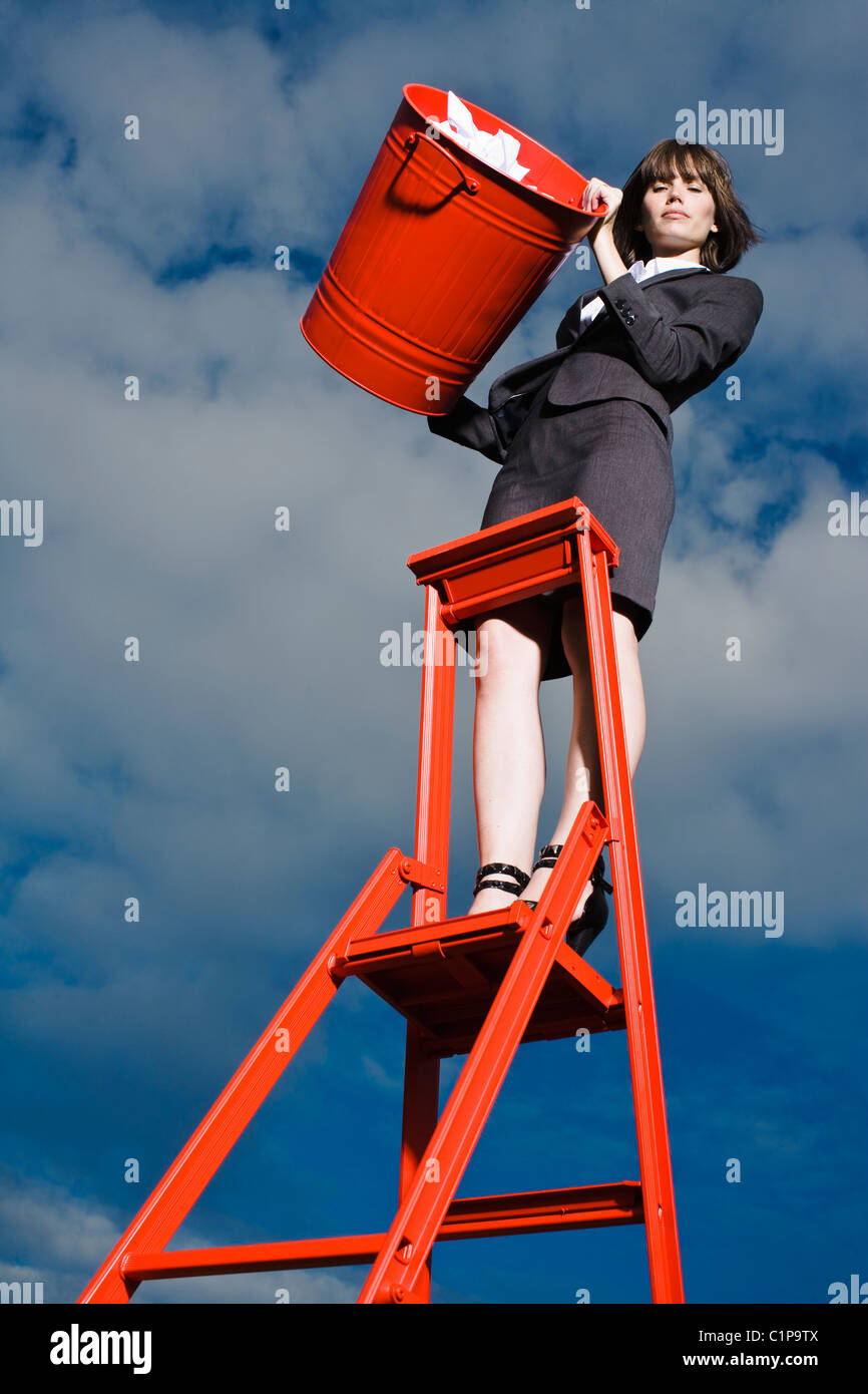 Woman throwing out rubbish from red bin standing on ladder Stock Photo