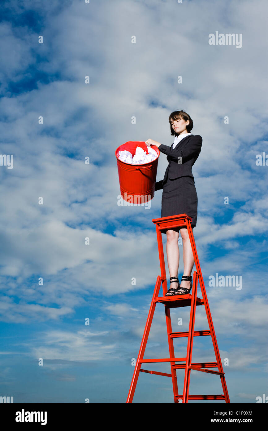Woman throwing out rubbish from red bin standing on ladder Stock Photo