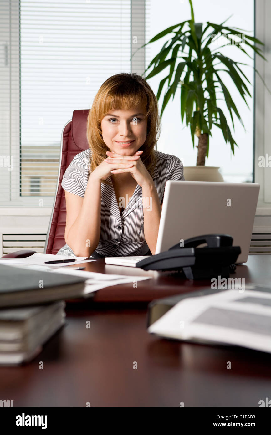 Photo of attractive woman sitting at workplace in the office and looking at camera Stock Photo