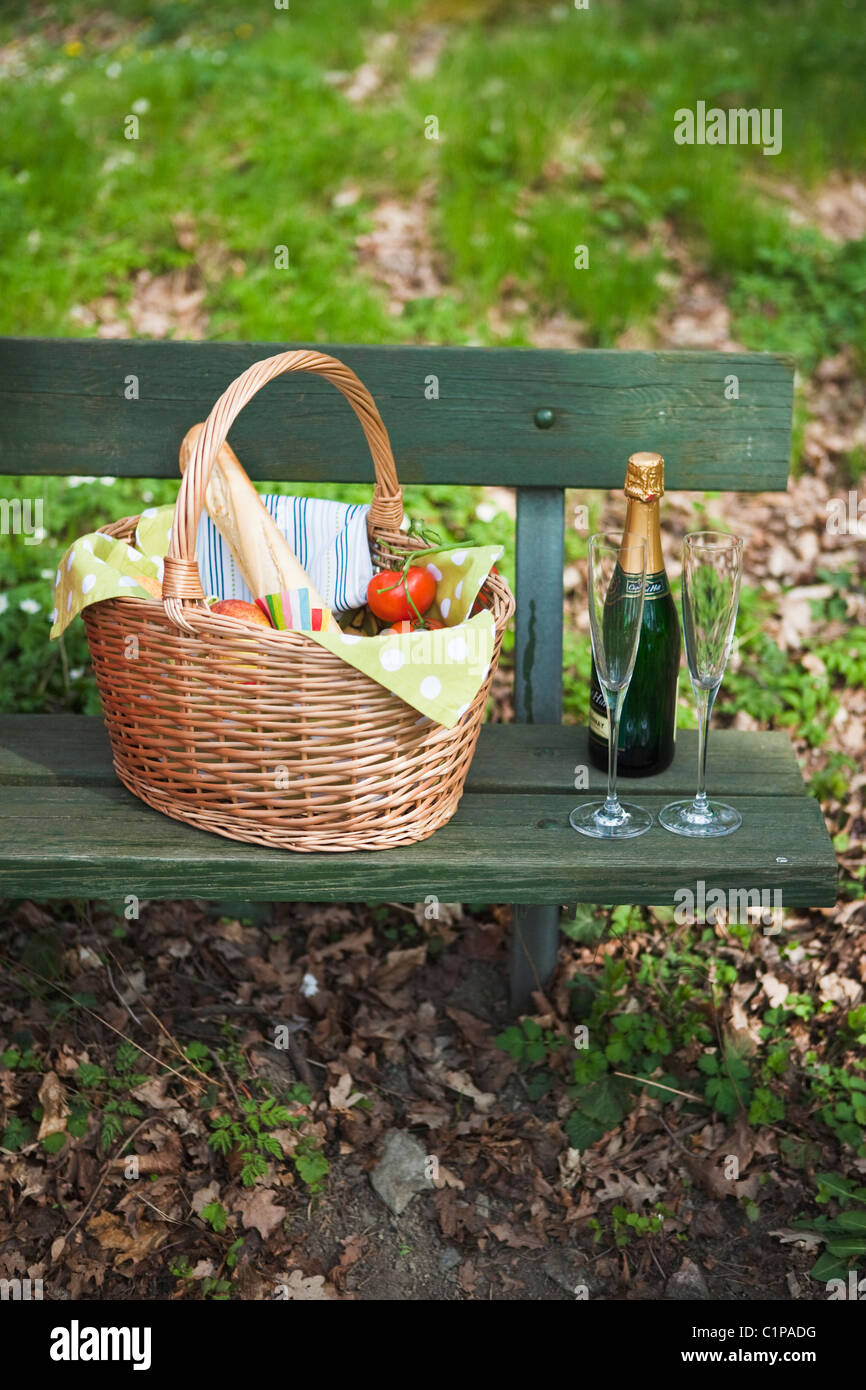 Picnic basket with champagne on park bench Stock Photo