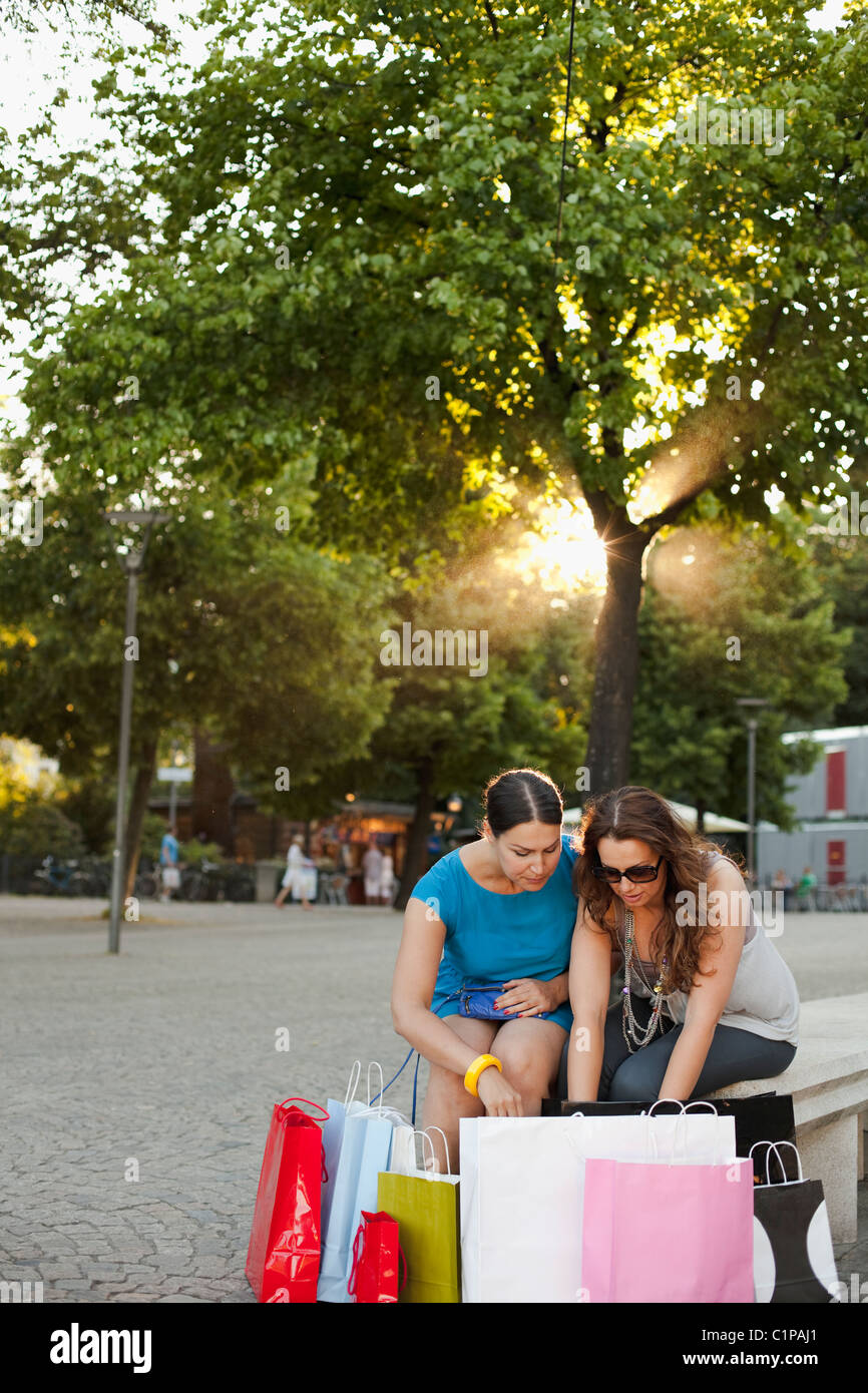 Two women sitting on bench and looking into shopping bags Stock Photo