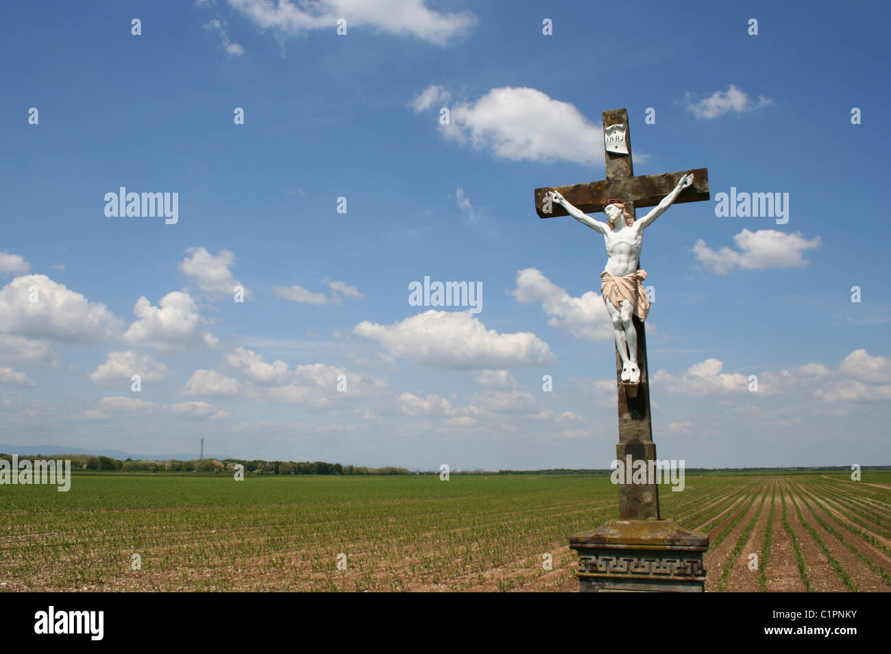 Alsace region, France. Statue of Jesus Christ on a stone cross stands in an empty field. Stock Photo