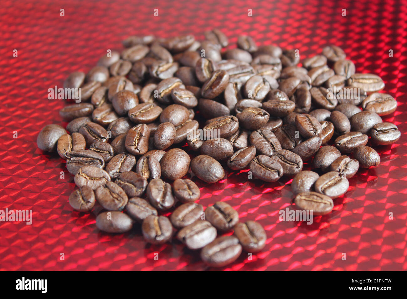 Roasted whole coffee beans scattered across a reflective red background