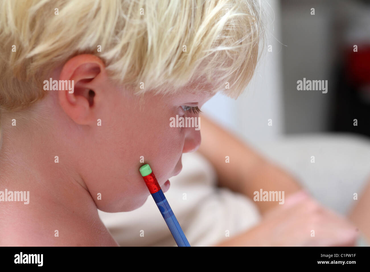 A young toddler or boy with light blonde hair concentrates on his homework with a blue pencil Stock Photo