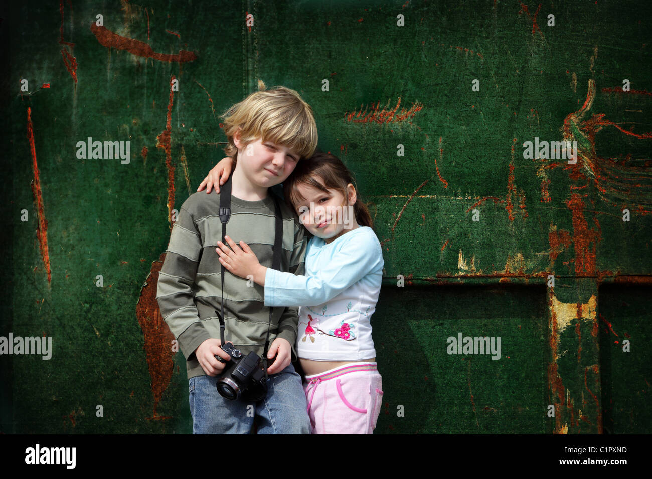 Two young children stand still while they have their photo taken against a grunge background and holding another camera Stock Photo