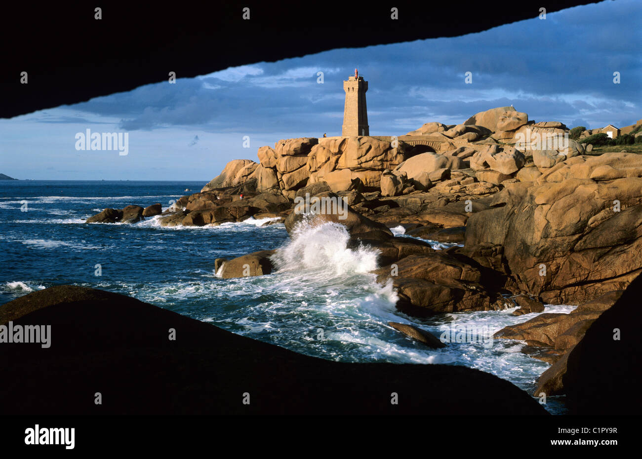 View through rocks to Lighthouse above stormy sea on the Pink Granite Coast. Stock Photo