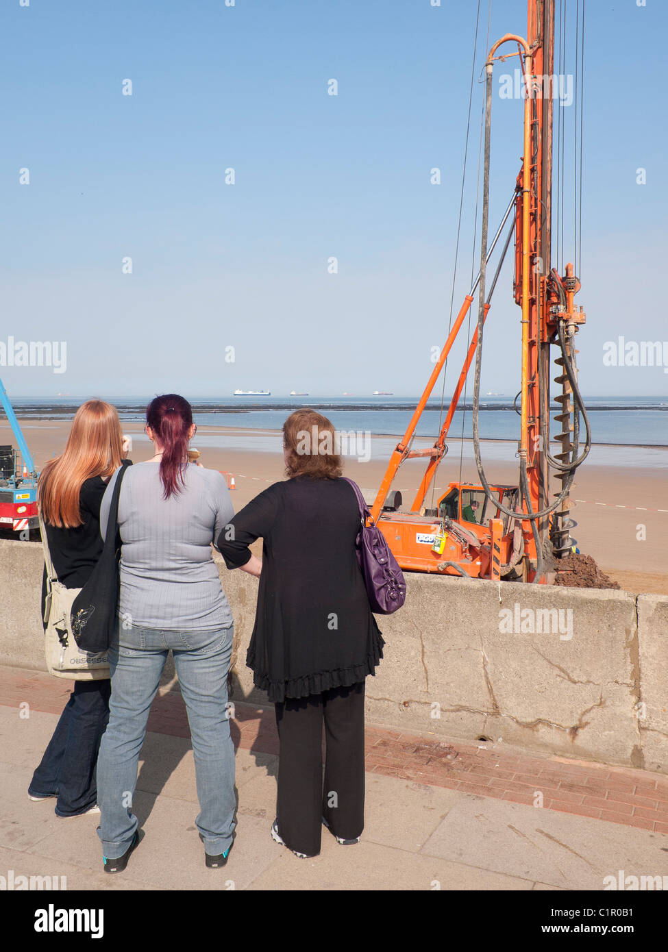 Three young women watching construction of a new sea wall on the beach at Redcar Cleveland North Yorkshire March 2011 Stock Photo